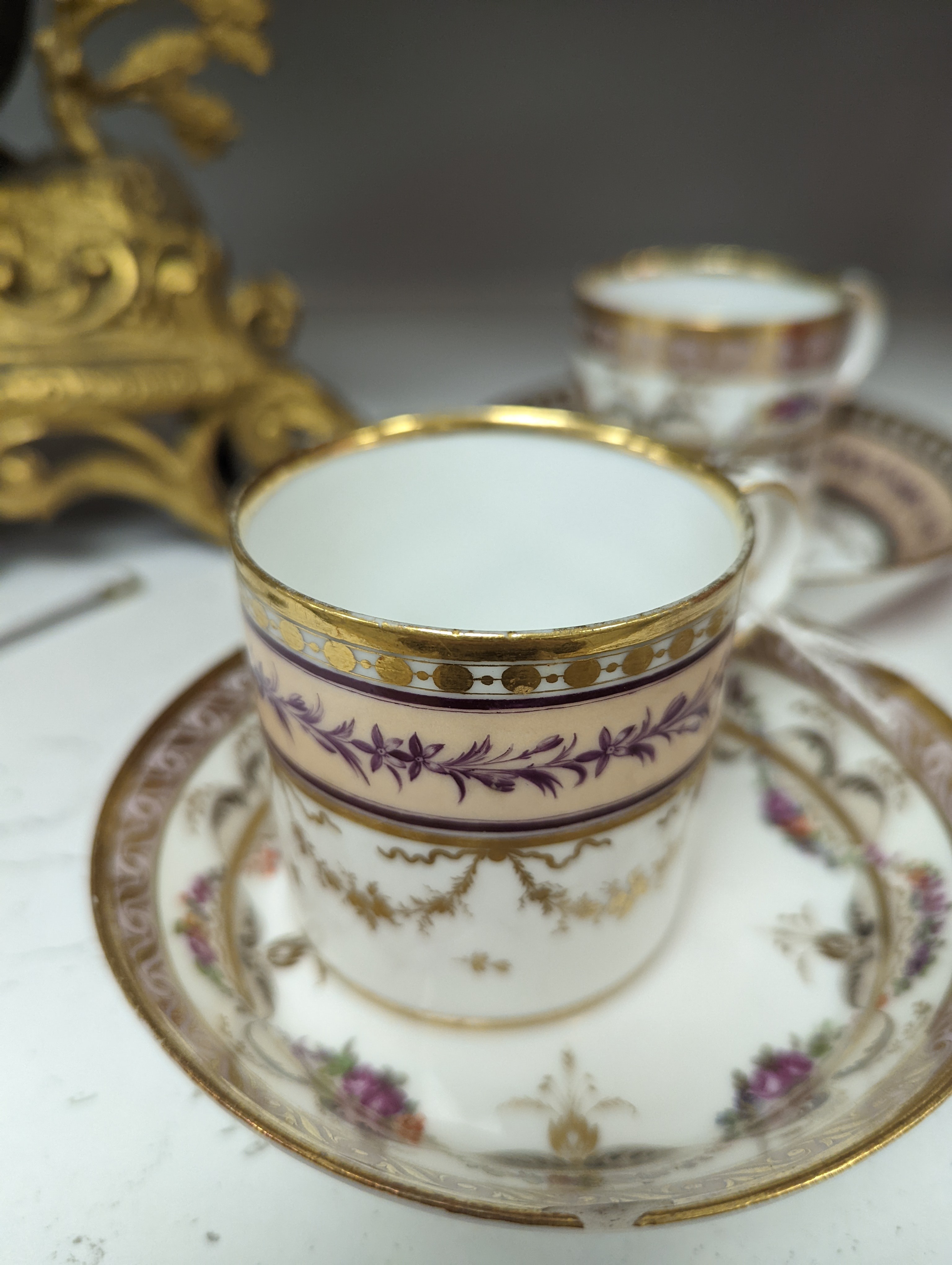 A Duc d'Angouleme coffee can and saucer painted with a puce chain of leaves on a salmon coloured ground and another painted with a flower chain, black feather and a gilt line, latter with stencilled red mark 'Manuf de M